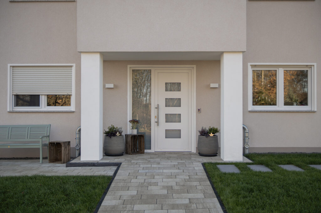 Eingangsansicht eines Neubaus mit weißen Fenstern und einer Haustür mit Seitenteil, Pflanztöpfe und eine Gartenbank, Nähe Erfurt